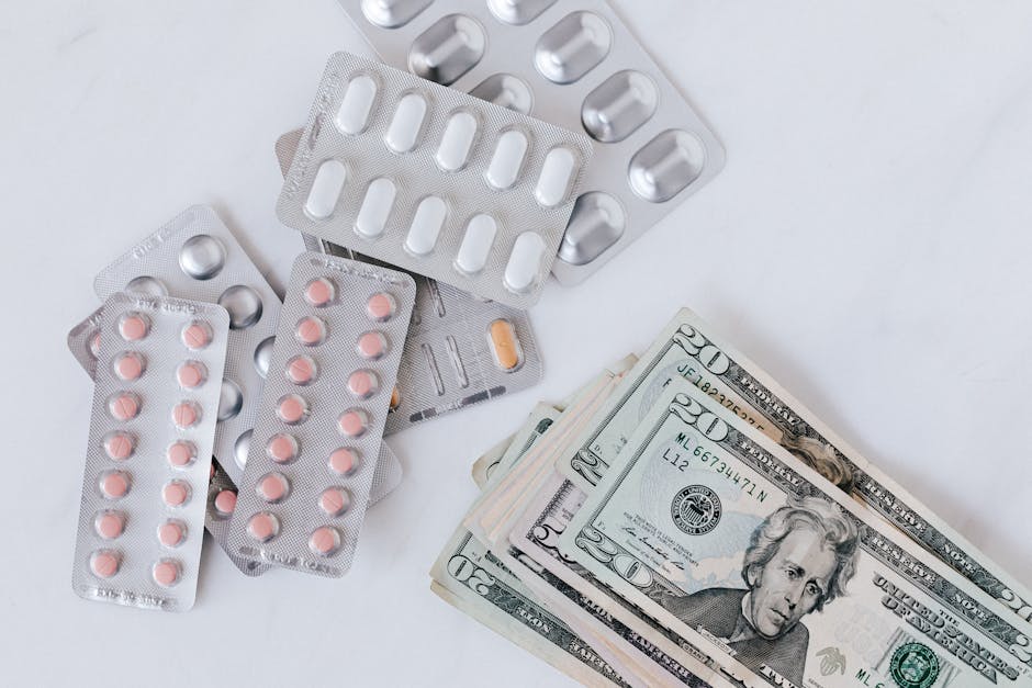 Several blister packs of pink and white pills, some empty and some with remaining medication, are scattered on a white surface alongside a small stack of US twenty-dollar bills, indicating a focus on 