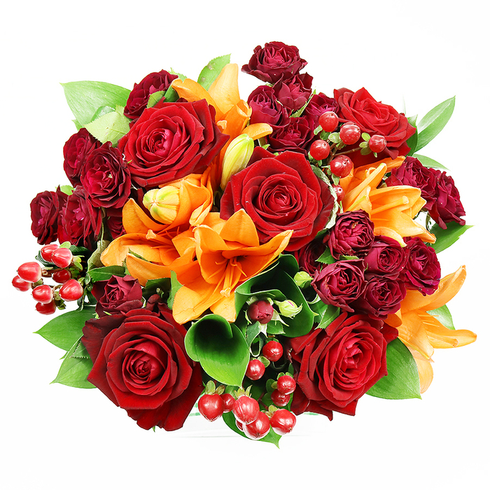 Captured from a top-down viewpoint on a spotless white field, this opulent floral arrangement is dense, circular, and meticulously balanced. Several large deep red roses take prominence; their velvety, fully unfurled petals create rich, shadowed hollows and convey a timeless romantic weight. Interspersed confidently are bright orange Asiatic lilies - unmistakable with their trumpet forms and visible stamens - some flung open to show their star-like faces, others gently unfolding to suggest freshness and unfolding promise. Nestled close to the focal roses are clusters of small, dark burgundy spray roses whose compact blooms provide a velvety, jewel-like texture that intensifies the bouquet's depth. Fresh green foliage, likely salal or ruscus, peeps between the flowers: broad, glossy leaves that cool the composition and sculpt the silhouette with organic curves. Glossy, spherical hypericum berries, a deep ruby tone, are scattered throughout, catching the light and offering lively textural contrast to the soft petals. The studio lighting is even and flattering, picking out petal edges and berry highlights while maintaining gentle shadows that grant a three-dimensional presence to the flat photographic plane. The sensorial suggestion is strong - the round, warming aroma of roses layered with a crisp, spicy hint of lily - so the bouquet reads as celebratory and intimate, suited for anniversaries, heartfelt apologies, or a thoughtful gift to brighten a home on Banbury Road or a cosy flat near Magdalen Bridge in Oxford.