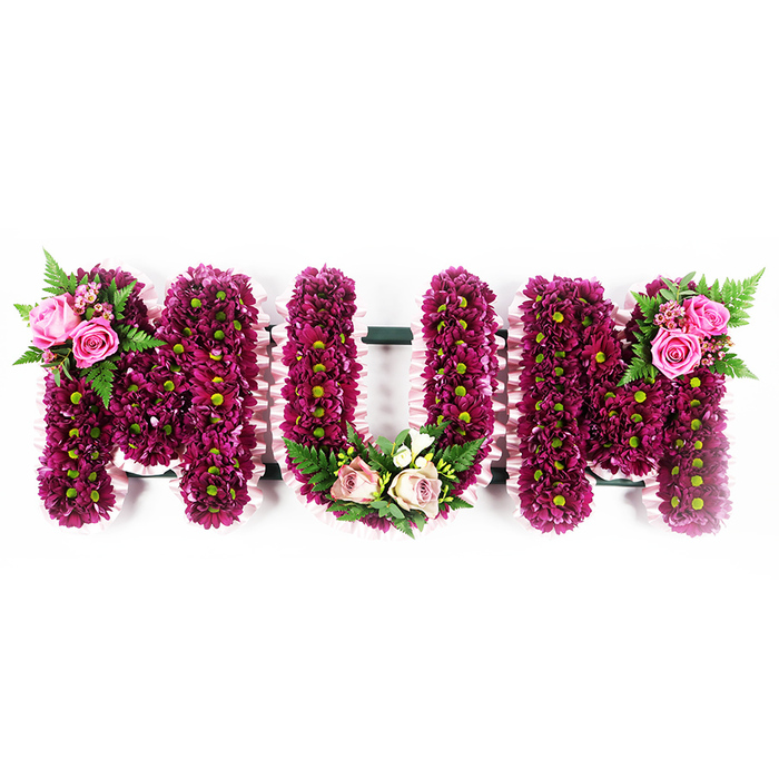 This photograph features a striking MUM floral tribute, created as three robust, standing letters, carefully posed against a crisp white backdrop so every petal and ribbon edge is clearly visible. The faces of the letters are thickly upholstered with small spray chrysanthemums in shades of rich magenta and deep purple, packed so tightly that they form a plush, almost cushion-like texture. Each blossom has a soft green centre, tiny yet distinct, giving the arrangement a lively, peppered effect that lightens the intense colour palette. The sides of each letter are edged with a delicate, ruffled light pink ribbon, which softens the strong shapes and suggests the gentleness and care associated with motherhood. On the upper left side of the first M, a cluster of open pink roses and partially unfurled buds rests among sprays of glossy greenery and arching fern, creating a focal point that draws the eye. The U is gently anchored at its base with a curved arrangement of blush pink and cream roses, combined with variegated foliage and fine white filler flowers that lend an air of serenity and calm. The second M repeats the visual rhythm with a matching group of vivid pink roses and fern fronds nestled into its upper right shoulder. The tribute feels thoughtful and crafted with intention, the kind of custom funeral arrangement that could be prepared by a local Oxford florist for a service near the Botanic Garden or along Iffley Road, designed to honour a beloved mother with colour, texture, and a quiet sense of celebration of her life.