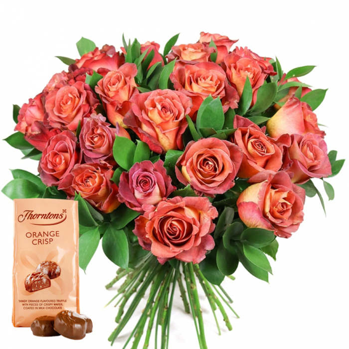 Dominating a pristine white backdrop, this striking image captures a voluminous bouquet of fresh roses-each petal painted with the delicate artistry of a local Oxford florist. The blooms flaunt their gradients: from subtle peach and sunlit yellow at their coiled centers, extending outward into lush shades of salmon, coral, and robust rosy pink, the colors reminiscent of tranquil evenings by the Cherwell. The petals appear velvety and close-packed, their fullness enhanced by a rich gathering of dark green foliage interspersed throughout-likely glossy ruscus or fragrant eucalyptus, echoing the foliage found within the University Botanic Garden. In the lower left, the bouquet is accompanied by a refined pouch of Thorntons Orange Crisp chocolates, a treat beloved in Oxfordshire. The soft cream packaging stands upright, its iconic Thorntons logo and the words 'ORANGE CRISP' bold and inviting, just above an appetising illustration of smooth chocolate truffles. The descriptive text promises a tangy orange truffle filling, studded with crispy wafer and enrobed in silky milk chocolate. Resting in front, two glistening chocolate truffles entice the senses, their glossy finish betraying their decadence. The bouquet's neat, green stems cascade downward, signifying floral freshness and expert preparation. Together, this pairing is an inspired gift-suitable for heartfelt occasions along the High Street, thoughtful gestures delivered to Summertown or Headington, or celebrations echoing the timeless romance of Oxford itself.