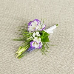 An elegant floral boutonniere rests on a subtly woven, light beige linen background, the soft, neutral fabric giving the piece a calm, refined presence. Two main lisianthus blooms draw the eye, their silky white petals edged with a deep, velvety purple that ripples around the ruffled tips, adding drama without overwhelming the arrangement. Tucked gently around them are clusters of tiny white filler flowers, similar to baby's breath, forming a light, cloud-like halo that brings a sense of softness and romance. Rising with quiet confidence through the design is a narrow stem of deep purple muscari, its tiny bell-shaped florets packed closely together, adding both texture and a saturated note of colour that ties the whole palette together. Nestled among the flowers are two pale green, unopened buds, promising future blossom and capturing that feeling of a day of celebration just about to unfold-much like the moment before guests arrive at an Oxford wedding venue along the River Thames or near Christchurch Meadow. Fine, feathery greenery, akin to asparagus fern, spills from behind the blooms in delicate fronds, giving the boutonniere a natural, almost meadow-like charm while still looking impeccably composed. The stems are gathered and wrapped in a smooth band of white satin ribbon, secured with a neat bow so that the piece can be pinned easily to a jacket lapel. The overall look is polished yet gentle, ideal for a groom, groomsman, or prom guest who wants their flowers to feel intimate and thoughtful. It's the sort of carefully considered buttonhole a local Oxford florist might prepare for same-day delivery to a city-centre hotel or a ceremony in one of the historic colleges.