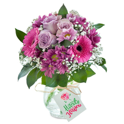 Evoking the quiet warmth of an Oxford afternoon, this luxurious mixed bouquet glows with nuanced pinks and purples-each bloom thoughtfully placed by a local florist who understands the unique charm of the city. Central to the arrangement are three to four roses in a gentle shade of lavender, their petals soft and untangling like the delicate folds on the spires that line the city skyline. Scattered purposefully among them are bold, cheerful Gerbera daisies in vibrant fuchsia pink, their faces turned outward as if greeting passersby along Cornmarket Street. Adding richness, clusters of magenta chrysanthemums with hints of plum bring texture, balanced by the light touch of white baby's breath, which drapes like morning mist over Port Meadow. The deep green foliage woven throughout provides structure and echoes Oxford's verdant parks. Displayed in a unique glass vase with subtle crackled detailing, the bouquet's presentation is completed by a rustic raffia ribbon tied around the neck. Attached is a simple white gift tag-a blank canvas for heartfelt messages, perfect for sending love or congratulations locally in North Oxford and Cowley. This arrangement, handcrafted with care and infused with the tranquil energy of the city, carries a sweet, gentle fragrance, making it a meaningful gift for moments that matter-whether celebrating a milestone or reaching out with kindness across Oxfordshire.