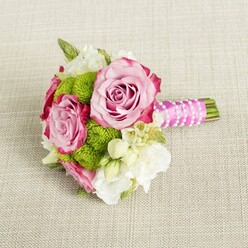 Laid gently across a pale, woven fabric that resembles fine linen in a soft beige tone, this small bouquet feels like a moment of calm before a celebration in Oxford's historic centre. Three pink roses anchor the arrangement, two of them fully open and prominently displayed, their petals shading from a tender, shell-like blush at the centre to more saturated, berry-pink edges. The outer petal rims carry a whisper of magenta, adding depth and creating a subtle, painterly ombré effect. Each rose head looks lush and full, the tightly layered petals suggesting both softness and strength, like the steady heartbeat of a wedding day. Clusters of bright lime green button chrysanthemums tuck in among the roses, their compact, rounded forms made up of many tiny, tightly packed florets. The green is vivid yet not harsh, bringing a lively contrast that keeps the design youthful and modern, much like a stylish celebration in Jericho or along Cowley Road. Around these key flowers, delicate white and cream filler blossoms weave through the bouquet - some appearing as small, star-shaped wax flowers with golden-yellow centres, others more ruffled and petal-rich, reminiscent of lisianthus or freesia. They soften the bolder colours and add an airy, almost cloud-like quality. The stems are carefully arranged and wrapped in a bright fuchsia pink satin ribbon, which gleams gently in the even, natural-looking light. Around this, a fine strand of white faux pearls spirals diagonally, like a bracelet slipped around the handle, lending a touch of bridal refinement. The green stem ends extend just beyond the ribbon, neatly clipped, reinforcing the sense of professional craftsmanship. Though compact, the bouquet suggests movement and emotion, ideal for a bridesmaid, a young bride, or as a sweet engagement posy, the kind of piece a local Oxford florist would craft for an intimate ceremony in a college garden or a reception tucked away near the High Street.