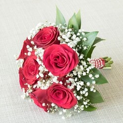 Resting gracefully on an off-white, subtly textured fabric, this exquisite Oxford bridesmaid bouquet weaves together the fiery passion of deep red roses and the pure innocence of delicate baby's breath. Each rose boasts velvety, richly saturated petals that spiral outward from a tightly closed core, their classic form evoking stories of romance sung beneath the spires of Oxford. Wisps of tiny, cloudlike white Gypsophila blossoms dance between the blooms, softening the bouquet's impact and adding a dreamy air, as if mirroring the mist that often settles over University Parks in the early hours. Sleek, glossy leaves-ruscus or salal-offer a splash of verdant green, peeking playfully from behind each blossom and giving the design lush depth. At the bouquet's base, the stems are collected with care and bound in a striking red and white ribbon, further distinguished by a spiral of glowing white pearls-an elegant nod to time-honored Oxford celebrations. The composition's visual rhythm, from textured backdrop to radiant flora, invokes a sense of graceful serenity, making this bouquet an unforgettable choice for anyone seeking to mark love, unity, or special moments amidst the historic charm of the Oxford community. Freshness and artistry shine through with every detail, inviting thoughts of tranquil gardens and cherished gatherings.