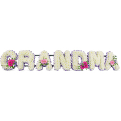 The image shows a carefully crafted funeral flower tribute spelling GRANDMA, the letters arranged in a graceful row as if gently resting in stillness. Every character is built on a sturdy frame then completely blanketed with snowy white chrysanthemums, their cushiony petals overlapping to form a soft, velvety texture. The blooms are fresh and full, suggesting that they were prepared the same day for a service somewhere in Oxford, perhaps near Headington or Summertown. A neat border of lilac ribbon runs around each letter, the satin edge catching the light and adding a refined, pastel halo that softens the strong shapes. Three focal points of colour draw the eye: dainty posies placed on the starting G, a central A, and the closing A. These miniature bouquets combine bright pink gerberas with their neat, daisy-like petals, smaller pink roses at different stages of opening, and sprigs of rich green foliage that curl and fan outward, bringing a touch of garden freshness. The greens echo the calm of college quadrangles and leafy streets off the Cowley Road, while the pinks bring a quiet sense of joy and gratitude. The overall lighting is gentle and diffused, allowing every curve of petal and fold of ribbon to be clearly defined without harsh shadows. You can almost imagine the soft rustle of stems being placed, the subtle fragrance of chrysanthemum and rose, and the hushed atmosphere of a farewell gathering. This floral lettering feels both strong and tender, a loving tribute arranged by an experienced local florist who understands the importance of honouring a grandmother with grace and beauty.