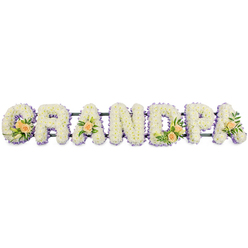 The image presents a beautifully composed funeral flower tribute spelling GRANDPA in bold, three-dimensional letters that stretch horizontally across the frame. Each letter is densely cushioned with small white chrysanthemums, their petals forming a uniform, velvety texture that looks almost like freshly fallen snow. Tracing the outer edges of the G, R, A, N, D, P, and final A is a fine outline of light lavender flowers, adding a soft lilac haze that gently separates the letters from the white background and lends a quiet, spiritual tone often appreciated for thoughtful services in Oxford's historic churches. At four points along the word, clusters of accent blooms bring warmth and individuality: the G and D each carry a small spray of peach roses, accompanied by slim white lily buds and sprigs of rich green foliage, while the first and last A are each adorned with a single peach rose and greenery. These touches of soft peach feel intimate and personal, like a private memory woven into the tribute. The entire word sits on a narrow, dark support bar, likely metal, which holds the letters in perfect line without distracting from the flowers themselves. Against the stark white backdrop, the tribute appears crisp, calm, and composed, ideal for resting at the front of a chapel or beside a photo at a memorial gathering in and around Oxford. The design balances formality with tenderness, expressing respect, remembrance, and enduring love for a grandfather who meant the world to his family.