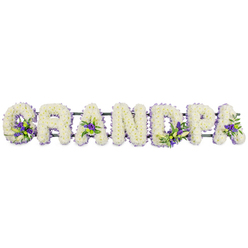 A large, horizontal floral tribute spelling out GRANDPA is presented against a bright white backdrop, every letter shaped with the calm precision of an experienced Oxford florist preparing flowers for a chapel near Headington or Summertown. Each capital letter is built on a hidden frame and completely carpeted with densely packed, small white chrysanthemums or carnations, their petals forming a cushion-like surface that radiates stillness and purity. The texture is soft and slightly domed, giving the word a sculptural quality, as though the letters have been gently carved from fresh snow. Around the edges, a neat outline of foliage subtly defines each letter, while selective accents of deep purple and lilac-toned blooms add depth. These violet touches, possibly lisianthus or petite irises, appear at the base of the 'G', in the open centres of the 'A's, along the stem of the 'D', and within the loop of the 'P', mingled with glossy green leaves to create small, comforting bursts of colour. Beneath the flowers, a dark green horizontal bar connects the letters, mostly obscured but essential for keeping the tribute steady for delivery to a funeral home or church in central Oxford. The arrangement has an air of hushed reverence, ideal for resting beside a coffin, at the lectern, or by a memorial photo. Its simple yet heartfelt design speaks of lasting affection, honouring a much-loved grandfather whose stories and presence shaped the family, and offering relatives a tender, personalised farewell that feels both local and deeply personal.