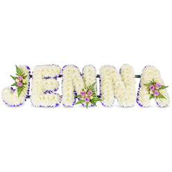 Lovingly crafted by local hands, this personalised tribute spells the name JENNA in large, three-dimensional block letters set against a clean white background. Each letter is formed from dense clusters of small, creamy white chrysanthemums or similar florets, creating a pillowy surface that invites quiet attention; the tactile bloom clusters catch light across their tiny petals, giving a soft luminosity to the whole piece. A slender purple ribbon or a fine line of lavender petals traces the interior edges of every letter, providing a refined definition that complements the pristine whites. The letters are joined by slim, dark structural bars that keep the design unified and ready to stand at a memorial or beside a coffin.

Deliberate accent clusters appear on the upper curve of the J, the lower mid-point of the second N, and the upper right of the A. Each cluster pairs blush-pink and pale lavender spray roses with small cream roses and fresh fern fronds, introducing warm, natural tones and a gentle rose fragrance that balances the chrysanthemums' clean scent. As an Oxford florist serving areas from Summertown down to Christ Church Meadow, Flowers Oxford prepares this design with calm attention to detail and local sensibility - a personalised floral name tribute chosen by families who want to honour memory with quiet beauty, available for careful local delivery across Oxford when needed for funerals, wakes, or remembrance services.