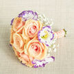 Captured from just above, this floral arrangement sits on a textured, light beige fabric that brings a quiet, natural backdrop to a composition of soft contrasts. At its core are plush apricot and peach roses, their petals rolled inward in tight spirals that gradually open into luminous cups, each showing subtle blushing tones of pink and warm orange. Nestled between them, white lisianthus bloom with ruffled petals, their edges traced in a lyrical violet-purple that sets a cool accent against the warmth of the roses; the small yellow stamens at their centres add a spark of brightness. Sprigs of baby's breath are artfully woven through the flowers, creating a delicate, cloudlike veil that breathes air into the bouquet rather than crowding it. The handle is wrapped in a matching blush ribbon and further embellished with fine rows of cream pearls, a tactile, refined detail that makes the bouquet comfortable to hold and flattering in photographs. The freshly cut green stems are trimmed neatly at the base, visible as a green anchor to the softer tones above. Bathed in soft natural light, the colours read clean and fresh - a palette that evokes the early morning calm of Oxford's Botanic Garden or a quiet lane off Cowley Road. The overall mood is romantic and composed, suited for weddings, intimate anniversaries, or as a thoughtful gift sent to someone across town, with the craftsmanship speaking to an experienced local florist's care.