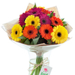 A cheerful cluster of Gerbera daisies in sun-bright yellow, bold orange, and lush magenta bursts with colour and life from a simple clear glass vase, capturing the vibrant spirit of Oxford's bustling marketplaces and leafy streets. The blossoms feature signature dark centres that create a striking interplay with the surrounding velvety petals, each flower radiating optimism like a bright morning on St Aldate's. Nestled among the daisies, fresh green leaves introduce depth and a soft, wild touch, while the wrapping-an artful combination of rustic brown kraft paper and translucent, softly crinkled cellophane-evokes both the organic charm of local florists and the contemporary touch of a modern Oxford bouquet. The neatly gathered stems, visible through the vase's pristine glass walls, are tied with a piece of textured twine, from which hangs a delicate white gift tag bearing a stylized red rose image that hints at care and personal sentiment. Illuminated by gentle, even lighting, the whole arrangement glows with a sense of celebration and warmth, making it ideal for occasions ranging from university graduations to heartfelt thank-yous. With every detail thoughtfully composed, this bouquet invites feelings of delight and gratitude, reflecting the excellence and community focus of Oxford's passionate local florists.