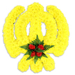 A large, vibrant floral tribute shaped unmistakably as the Sikh Khanda fills the frame against a pristine white backdrop, every curve and line rendered in sunlit yellow. Hundreds - perhaps thousands - of small, tightly packed bright yellow chrysanthemum blooms form the emblem's circular chakkar, the upright double-edged khanda and the two curved kirpans, their compact petals creating a plush, almost quilted texture that catches soft studio light and throws a gentle shadow beneath. Set at the very heart of the symbol is a concentrated cluster of deep red roses, five or six buds arranged close together so their velvety petals read as a single, dramatic point of focus; they are cushioned by sprigs of dark green fern, whose feathery fronds frame the roses and add a cool, leafy contrast to the warm yellow. The overall effect is at once bold and tender - ceremonial in its accuracy, intimate in its finish - suggesting a floral piece intended for remembrance, a memorial service, or a gathering that honours Sikh faith and community. There is a faint, natural perfume: a green, floral top note from the chrysanthemums with a richer, fuller rose scent at the centre, implying recent conditioning and careful handling by hands that know their flowers. As a local touch, this would sit respectfully at events across Oxford - from a service near the Covered Market to a community remembrance in Jericho - and its clean presentation on white emphasizes both reverence and the artisan craft behind the design.