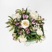 Viewed from directly above against a clean, brilliant white background, this hand-tied bouquet glows with the quiet elegance of creamy white and soft ivory roses, each bloom at a different stage of opening so you can almost feel the petals unfurl. Some roses are still cupped, with a hint of pale yellow at their core, while others spiral fully open, revealing intricate layers that look as though they have been gently turned by hand. Threaded between these classic blooms are alstroemeria in purplish-pink and lavender tones, the kind of Peruvian lilies you might see at their freshest on an early morning stroll past Oxford's Covered Market flower stalls. Their slender buds and partially unfurled petals show delicate streaks of green and berry-pink, giving the arrangement both movement and contrast without overwhelming the calm palette. Tiny white gypsophila, or baby's breath, drifts between the larger flowers like soft clouds, softening every edge and adding a gauzy, romantic lightness. A rich collar of deep green foliage, broad and glossy, cradles the blossoms and anchors their brightness against the white ground, suggesting the kind of lush, just-cut freshness you'd expect from a bouquet prepared the same day. The lighting is bright but gentle, without harsh shadows, so every petal texture and leaf vein is easily read, creating a sense of serene clarity, like soft daylight filtering through an Oxford townhouse window. The overall feeling is refined and heartfelt, an arrangement that would be equally at home welcoming a new baby in Headington, marking an anniversary near Summertown, or offering a tender, dignified tribute in times of quiet remembrance.