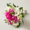 A showstopping bouquet, gathered by an Oxford florist for weddings or vibrant occasions, sits illuminated by gentle afternoon light, its hand-tied stems resting on a neutral, textured cloth. The central feature is a gathering of bold fuchsia peonies, their extravagant ruffles full and lush, surrounded by sprays of pristine white Alstroemeria-each one offering slender, trumpet-like petals lightly stroked with maroon patterning. Sprigs of bright green spiked buds-perhaps Veronica or young Hyacinth-rise between the main blossoms, bursting with fresh colour and lively structure reminiscent of blooms found in the Oxford Covered Market. Smaller white, bell-shaped flowers fill the spaces, softening the arrangement's rich vibrancy and ensuring textural balance. Deep green leaves anchor the bouquet, peeking out from beneath and reinforcing the design's layered depth. Everything is gathered tidily and finished with a striking pink satin ribbon, ready to be carried down the aisle of an Oxford college chapel or to brighten a celebratory event at The Randolph. The arrangement's joyful palette and tactile mix invite admiration, capturing both the romance and the contemporary spirit of Oxford's floral artistry, perfect for spring celebrations and elegant gatherings throughout the city.
