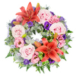 A richly detailed circular wreath is displayed on a spotless white background, its flowers forming a gentle yet striking tribute that would look at home at a funeral or remembrance gathering anywhere in Oxford, from Cowley Road chapels to quiet services near Headington. The eye is immediately drawn to two bold Asiatic lilies in deep coral-orange, one opening along the top of the ring and another echoing it nearer the bottom. Their broad petals, each with subtle shading and a soft sheen, cradle dark stamens at the centre and bring a sense of warmth and courage to the arrangement.   

All around them, clusters of full-blown roses in blush and light pink-lavender tones nestle closely together. Their many petals, unfurling in tight spirals, give the wreath a plush, velvety look that feels comforting and serene. Interwoven through the roses are lisianthus blooms in soft pink and rich purple hues; their ruffled, cup-shaped petals add movement, as though the flowers were gently stirring in a quiet breeze. Fine sprays of tiny lavender-blue filler flowers, reminiscent of statice, weave through the design, creating a soft, mist-like texture and linking one cluster of blooms to the next.   

Blue-grey eryngium thistles add a distinctive, spiky contrast, their cool tones echoing the calm of an overcast Oxford sky. Beneath the blossoms, the wreath is underpinned by layered greenery: silvery eucalyptus leaves, feathery ferns, and deeper green foliage provide a strong, natural base. Bright green folded leaves, carefully shaped near the lilies, give the design a precise, contemporary touch. A few unopened lily buds are tucked among the foliage, hinting at life and remembrance continuing beyond the ceremony, and completing a tribute that speaks of enduring love and respect.