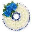 This image shows a bespoke funeral tribute crafted into the precise shape of the number '0', photographed from above against a pure white background so every detail reads clearly. The base is formed from hundreds of small white spray chrysanthemum florets, densely arranged to create a soft, pillowy surface whose layered petals suggest quiet comfort and serene purity. Around both the outer and inner edges of the numeric form a pleated, royal blue satin ribbon is carefully applied, its scalloped ruffles mirroring the curve of the '0' and lending a refined, almost ceremonial border that echoes the deep blue of the roses. At the upper left curve a focused cluster of three royal blue roses sits slightly raised, their velvety petals unfurling from tight centers and drawing the eye with a jewel-like intensity; a few glossy, dark green leaves tuck in behind them, giving natural depth and a subtle contrast to the cool palette. The lighting is soft and even, casting gentle shadows across the chrysanthemum texture and bringing out the ribbon's satiny sheen without glare. This numeric tribute reads as an intimate and personal memorial accessory - often commissioned to mark a particular age or a meaningful figure in a life being remembered - and its colour choices of white and deep blue convey respect, calm, and lasting remembrance. As a local florist in Oxford, we design these pieces with attention to both tradition and personal meaning, and the arrangement is composed to sit gracefully on a stand or easel at a memorial service, evoking the quiet dignity appropriate to wakes or funerals across the city and surrounding communities.
